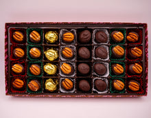 Box of assorted liquor chocolates with different shapes and colors on a light pink background