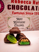 Chocolate mint candies with a mint leaf in front of a Rebecca Ruth Chocolates box.