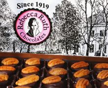 A box of Rebecca Ruth chocolate bourbon balls with a pecan on top, displayed in front of a graphic with a house and trees in the background.